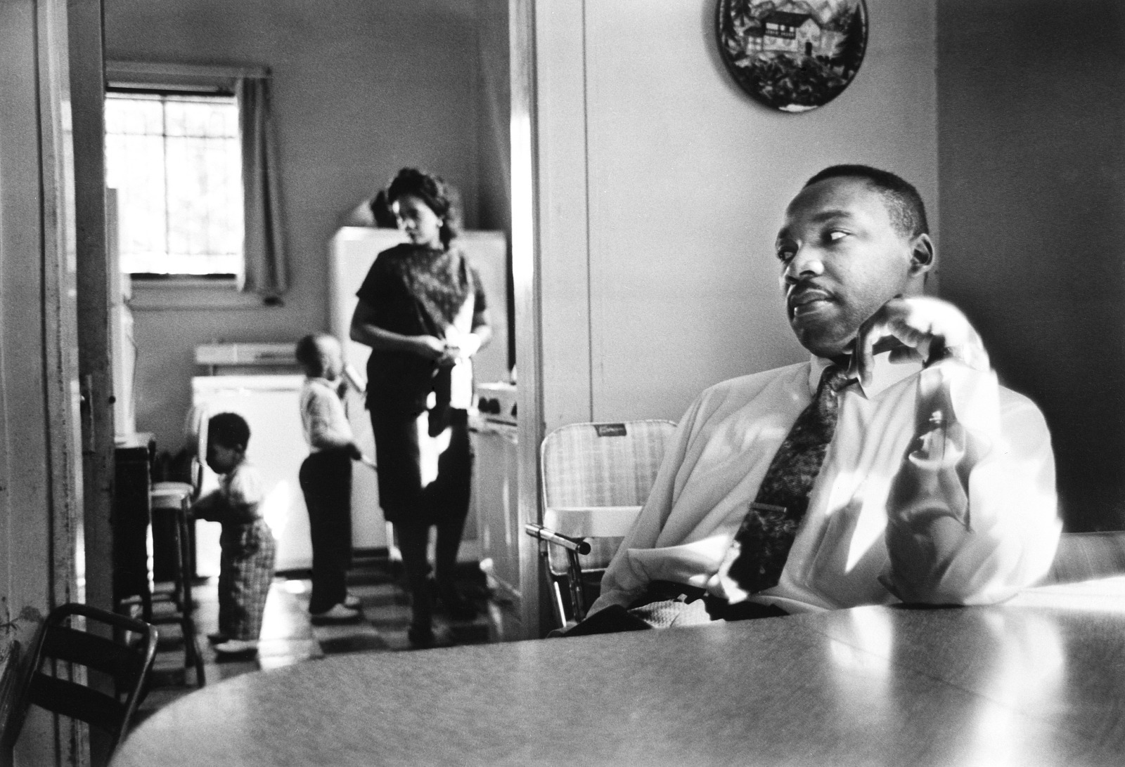 Black and white photograph of Dr. Martin Luther King, Jr., sitting at a table with his wife, Coretta Scott King, and two children in the background