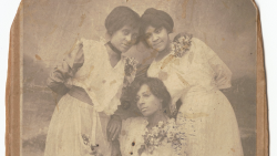 Black-and-white portrait-style photograph from 1915 of three young Black women wearing light-colored dresses with corsages pinned to their bodices and leaning against each other